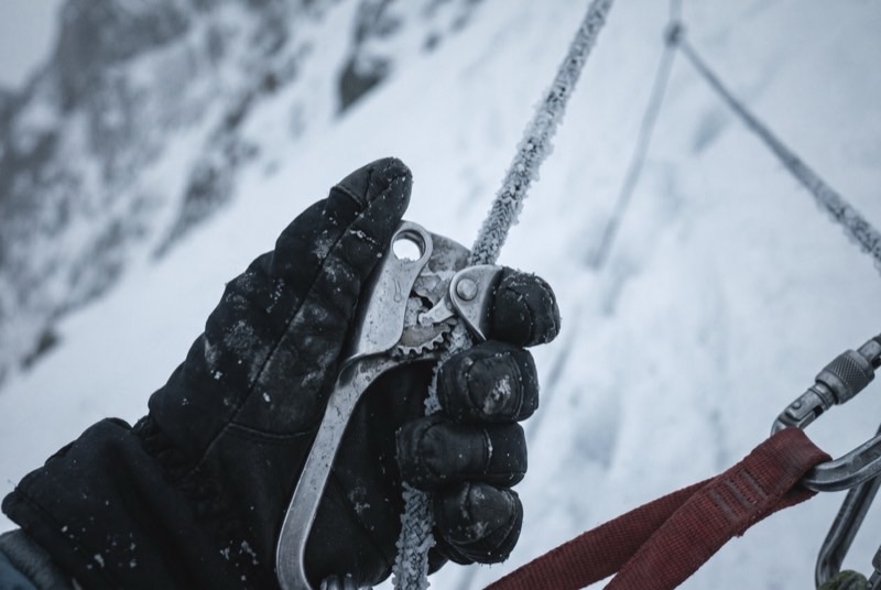 A gloved hand gripping a rope ascender clamped to a frost-covered fixed line on a steep snow slope