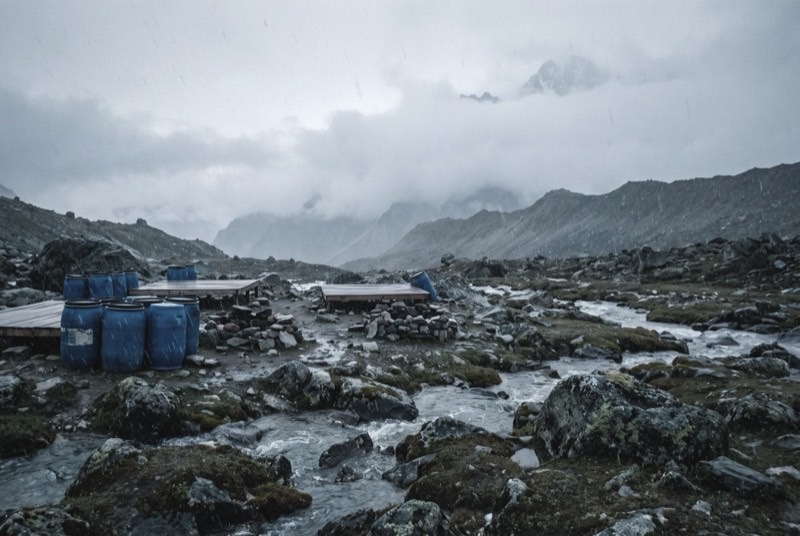 An empty high-altitude expedition base camp on grey glacial moraine, the ridges behind swallowed by cloud.