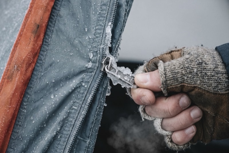 A gloved hand straining at a tent zip frozen solid with rime ice.